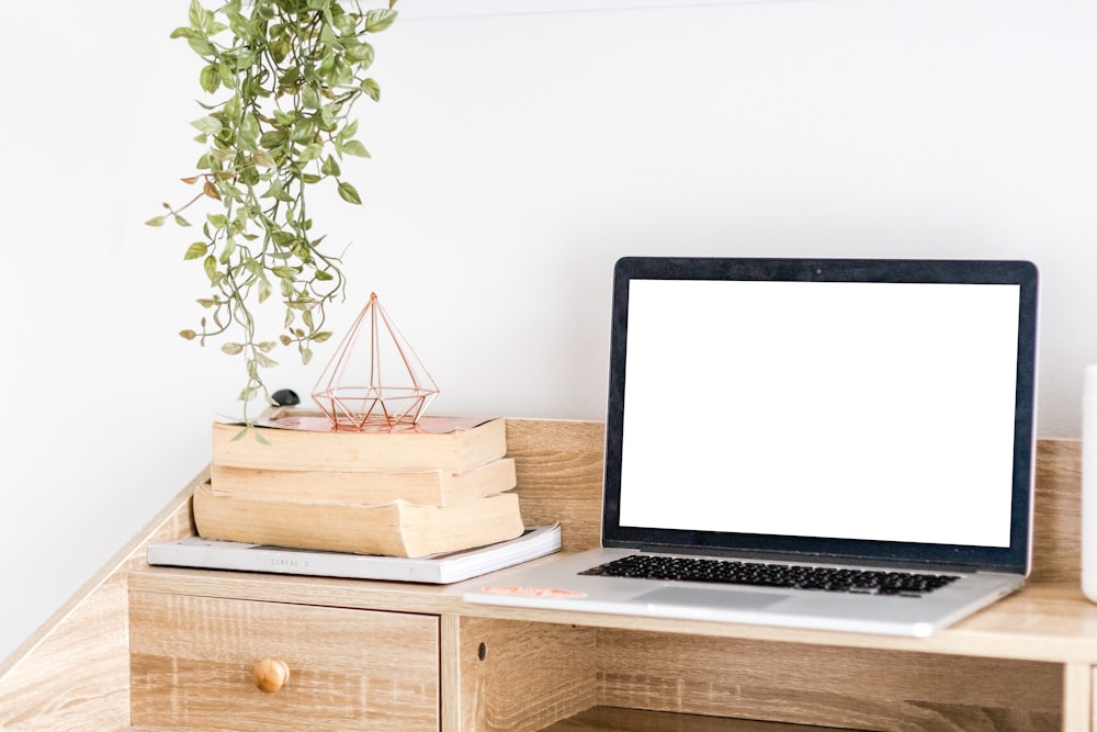 MacBook argenté sur un bureau en bois près du mur