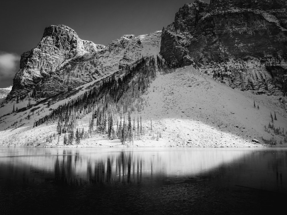 grayscale photography of calm lake by mountain