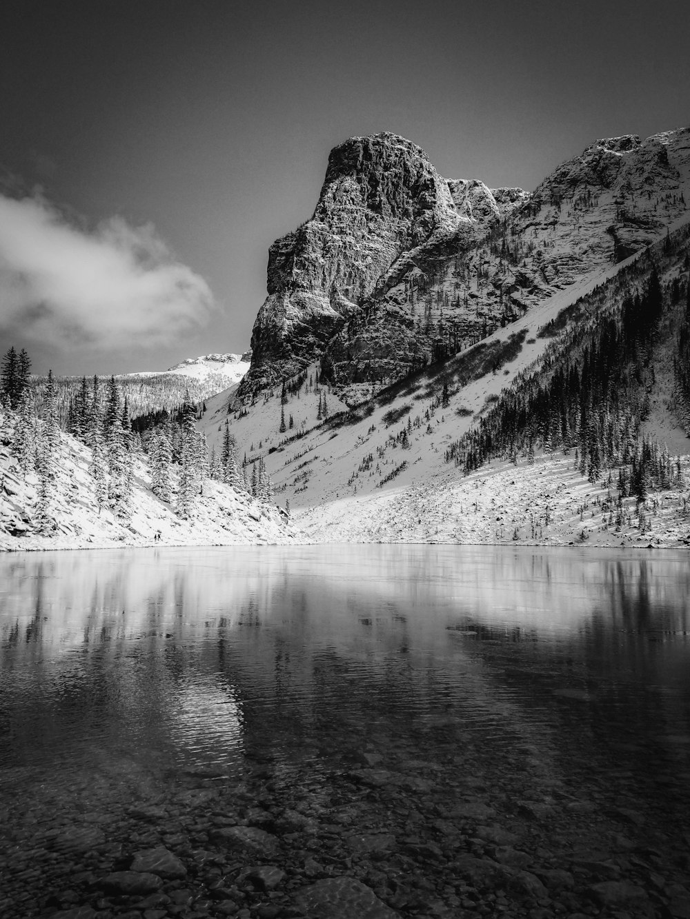 grayscale photography of calm body of water by mountains