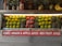 A fruit display featuring neatly arranged rows of pineapples, citrus fruit, pomegranates, and a few bananas on the side. Two juice bottles are also visible on the shelf. A sign below advertises various fruit juices like Shake, Anaar (pomegranate), Apple Juice, and Mix Fruit Juice.