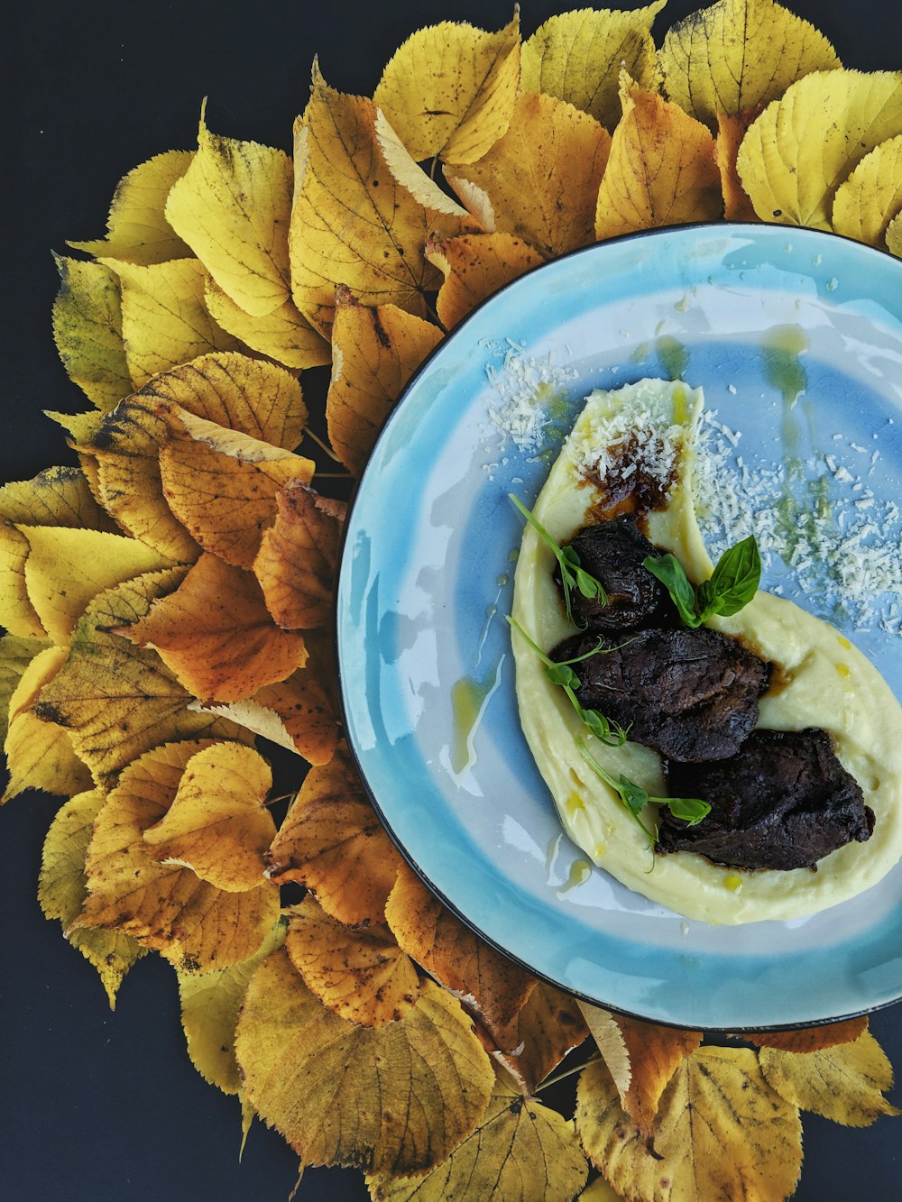 a blue plate topped with food on top of a leaf covered table