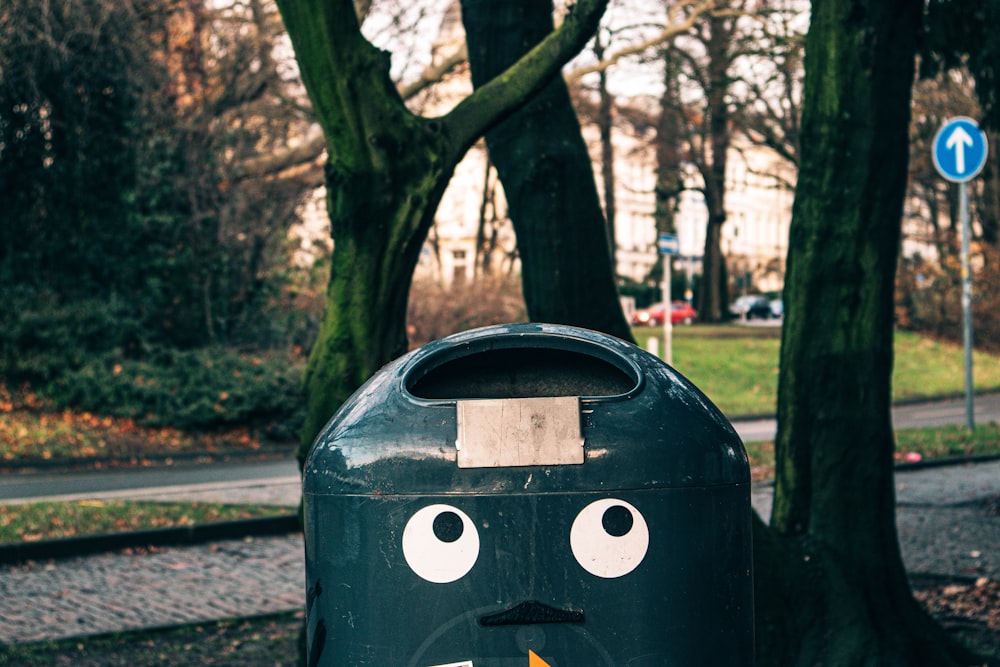 green outdoor garbage bin with face near tree during daytime