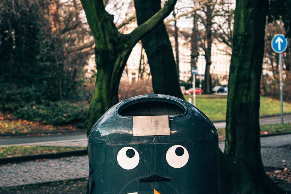 Cubo de basura verde al aire libre con cara cerca del árbol durante el día