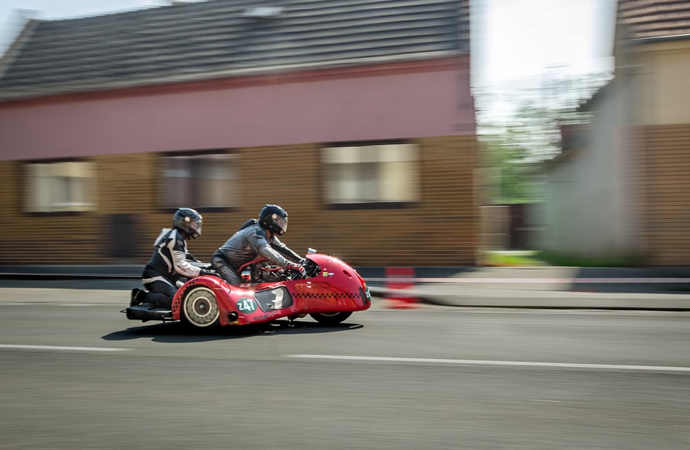 panning photography of red 3-wheeled vehicle with two person riding on