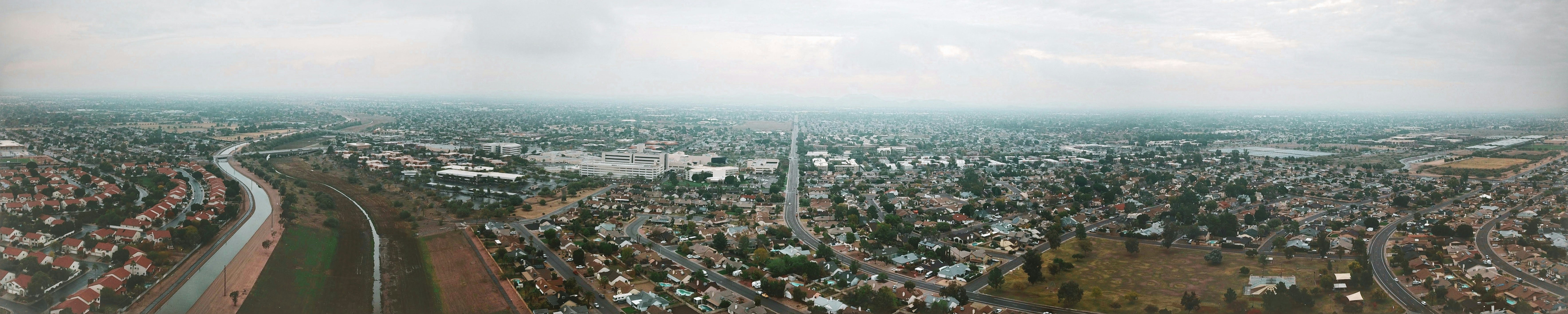 Panoramic view from the sky overlooking neighborhoods, recreational park, canal, bridges, shopping centers, a hospital, and medical center.