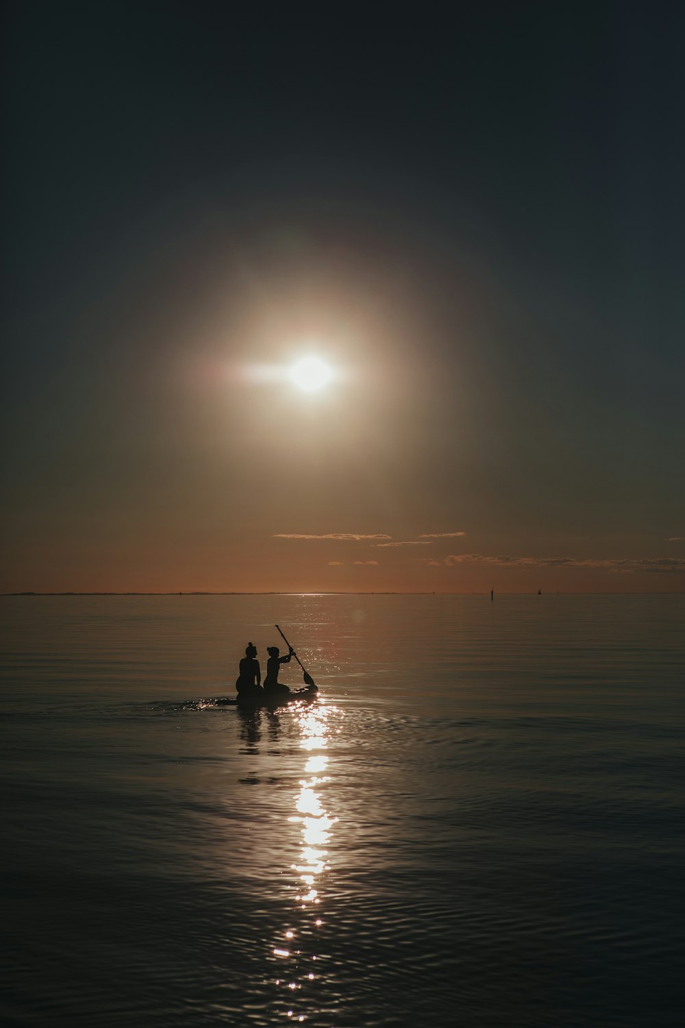silhouette of two person riding on boat in calm body of water under the sun
