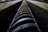 A close-up view of a large, industrial screw thread situated between two metal tracks. The focus is on the textured, rusted surface of the thread, conveying a sense of industrial machinery and wear over time.