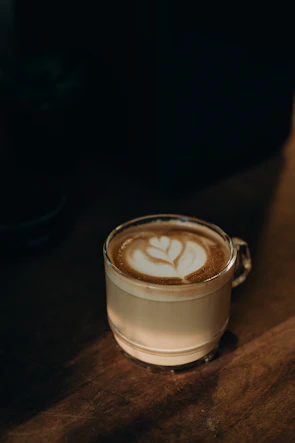 A creamy coffee latte with intricate latte art in a clear glass, sunlight highlighting the foam.
