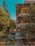 A mid-rise building with multiple balconies and a tiled roof is surrounded by lush greenery, including tall pine trees and dense shrubs. The architecture features wooden accents, and the area appears well-maintained with pathways and a small garden in front.