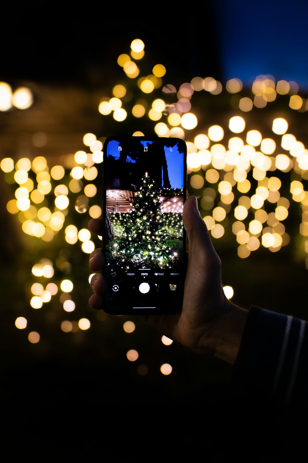personne tenant un smartphone noir prenant une photo d’un arbre de Noël vert