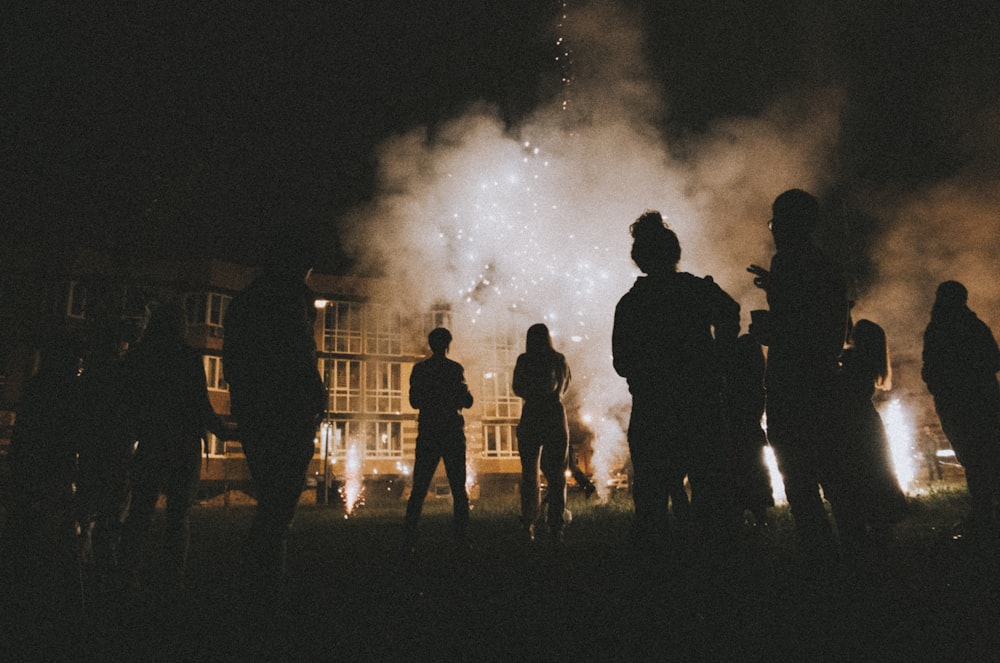 silhouette photography of people standing near smoke and building during nighttime