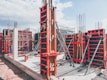 A construction site with multiple concrete formwork structures in place. Metal braces and supports are prominently visible, ensuring the stability of the forms. Concrete foundations and vertical columns are being prepared, with a mix of exposed rebar and newly laid concrete. The overall environment appears organized and active, reflecting ongoing building activities.