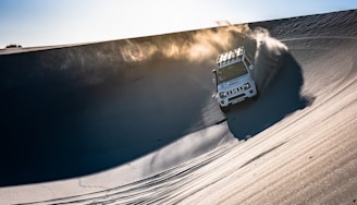 Dune Master ATV cresting a steep sand hill with the setting sun behind.