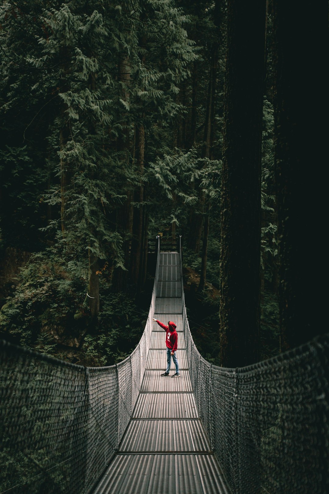person wearing red hoodie standing on the hanging bridge