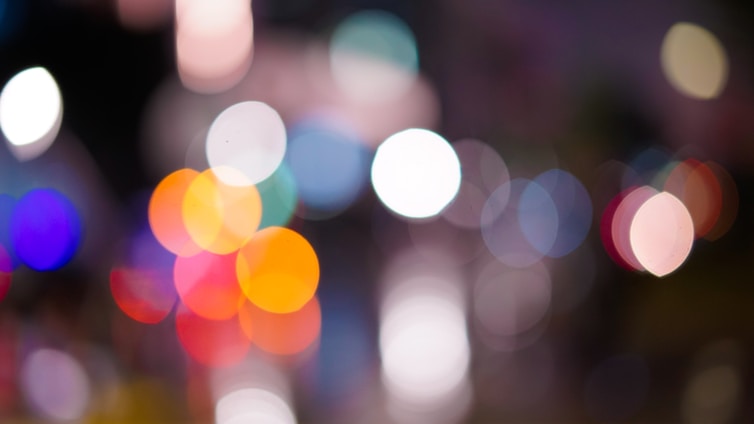 A blurry abstract photograph with circular light patterns in various colors. The lights are out of focus, creating a bokeh effect with shades of red, orange, blue, white, and purple.