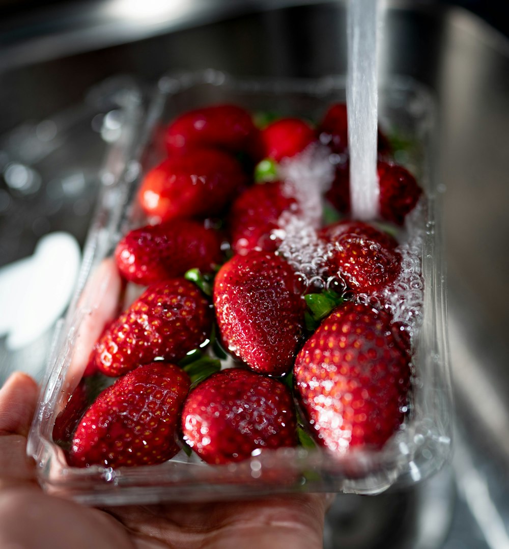 water poured into red strawberries in plastic tray