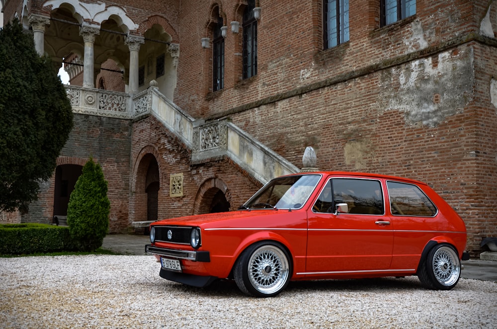 red fastback vehicle parked beside wall