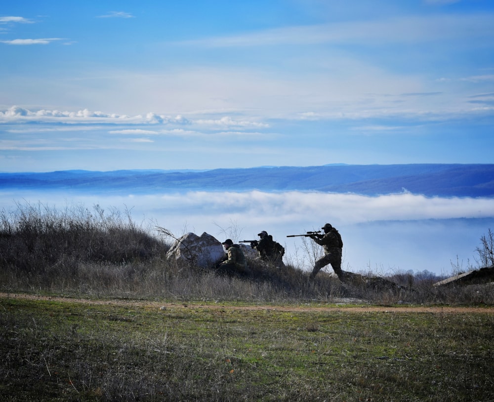 silhouette of people using rifle walking on grass field