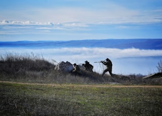 silhouette of people using rifle walking on grass field