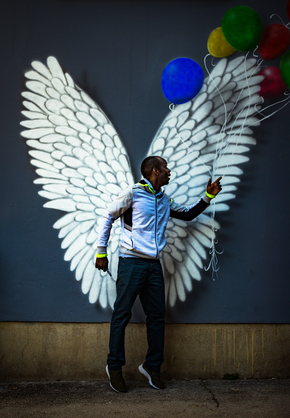 homem em pé na frente de asas brancas e balões de cores variadas grafite na parede