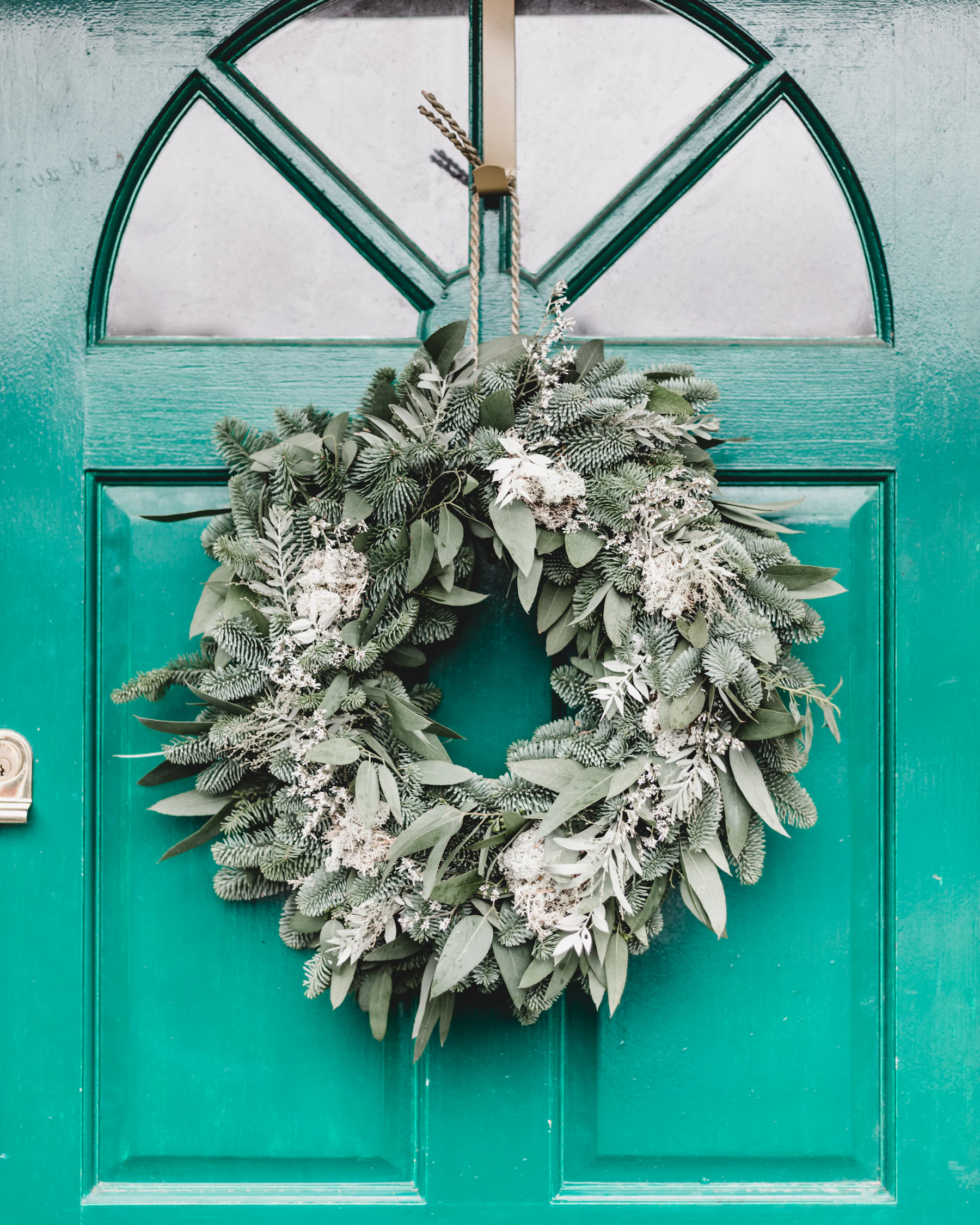 A full wreath of fir and eucalyptus hung by a cord on a green paneled front door