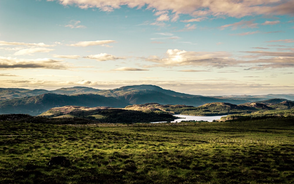 landscape photography of green field and mountains under a cloudy sky