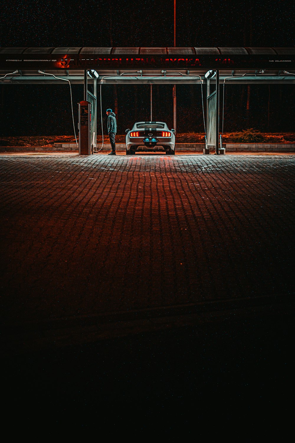 man standing near gasoline station beside vehicle during night time