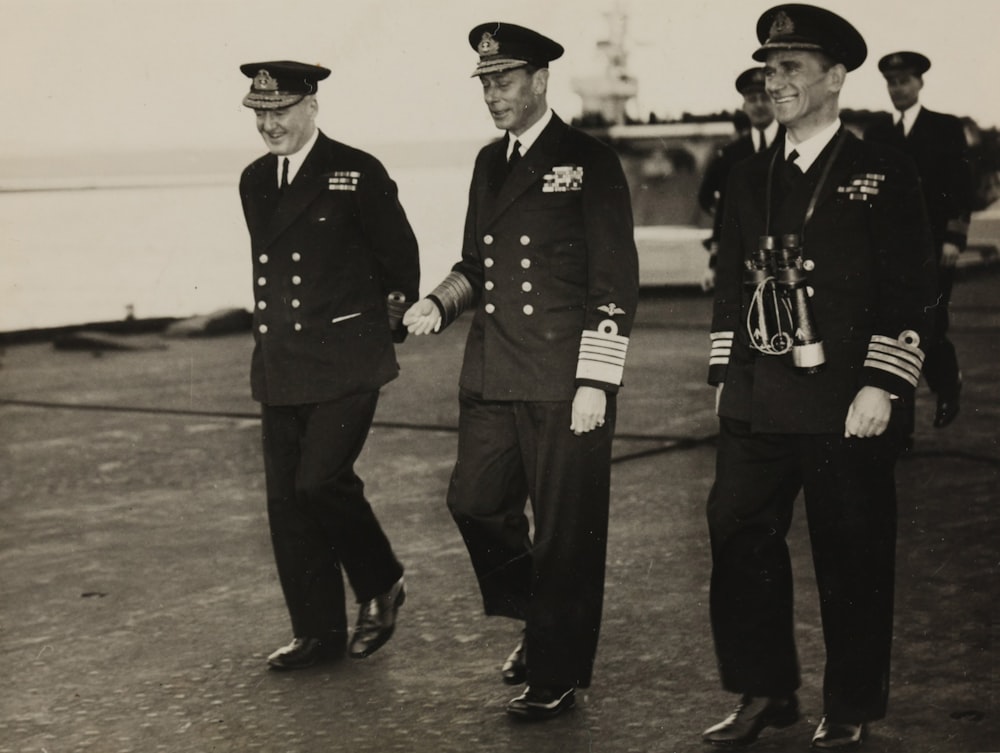 grayscale photo of three men walking on concrete pavement