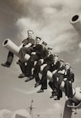 Veteran sailors standing together on a ship deck under a navy blue sky.