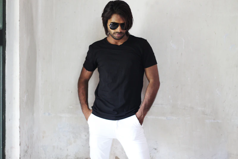 man in a black shirt and white pants standing by a wall