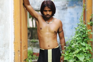 topless man leaning on brown wooden wall