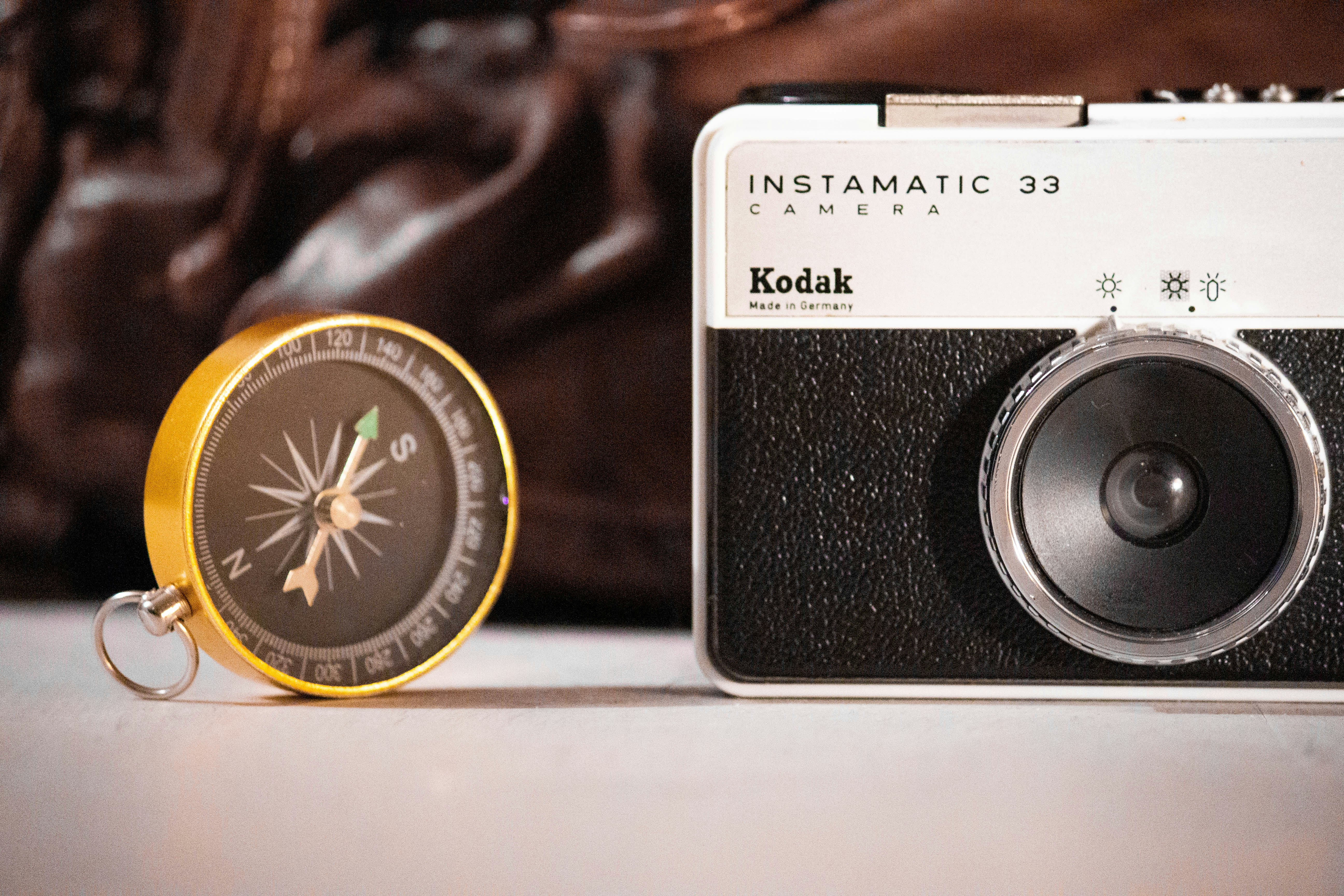 黒と白の Kodak Instamatic 33 カメラと丸い黒と金のコンパスの写真 Unsplashで見つけるコダックカメラの無料写真