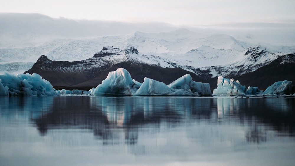 reflection of snow mountain on body of water under white sky