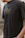 A person wearing a black t-shirt with a gold outline graphic of a mythological or spiritual figure in a meditative pose. The image captures the upper torso and partial arm of the individual in an outdoor setting.