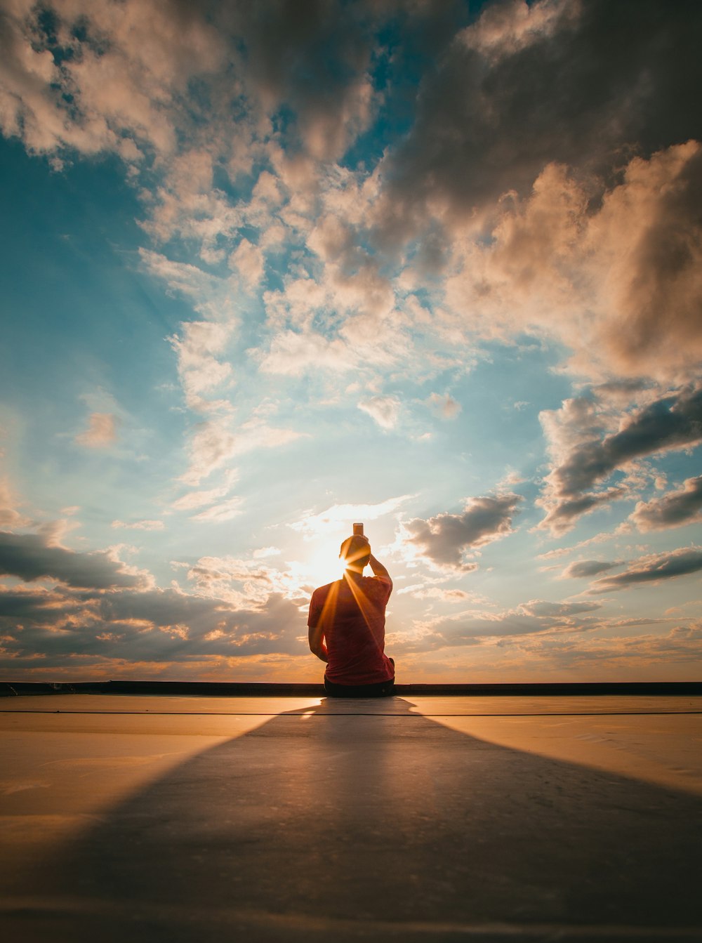 person sitting and facing back under blue and white sky