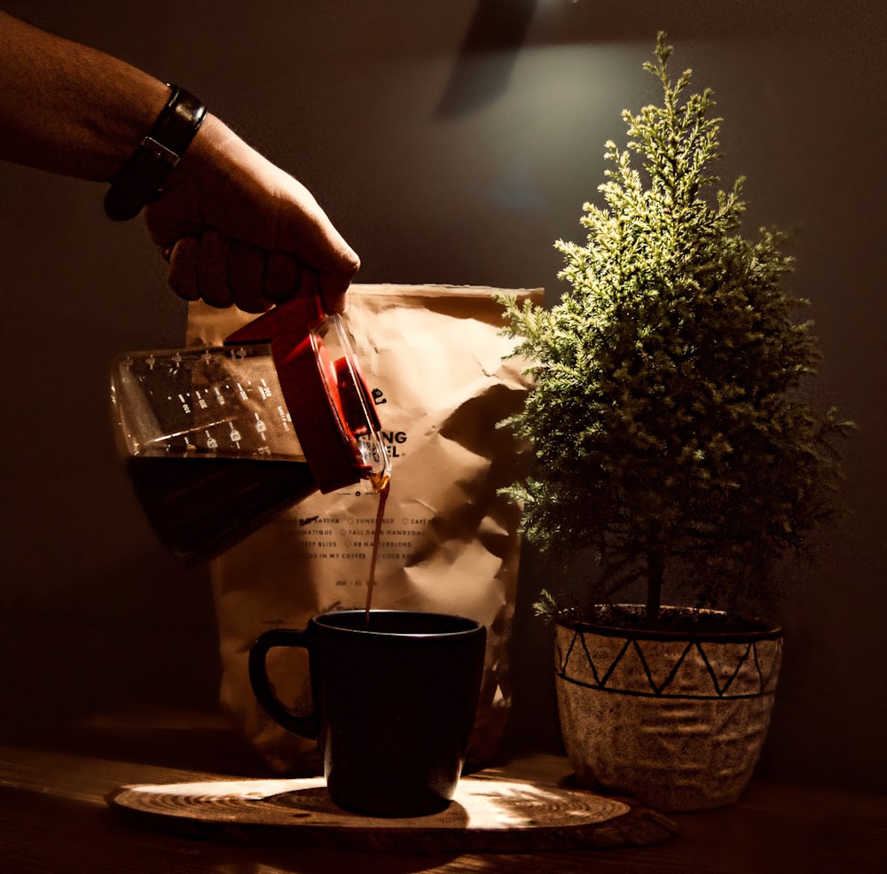 person pouring coffee in black ceramic mug on table