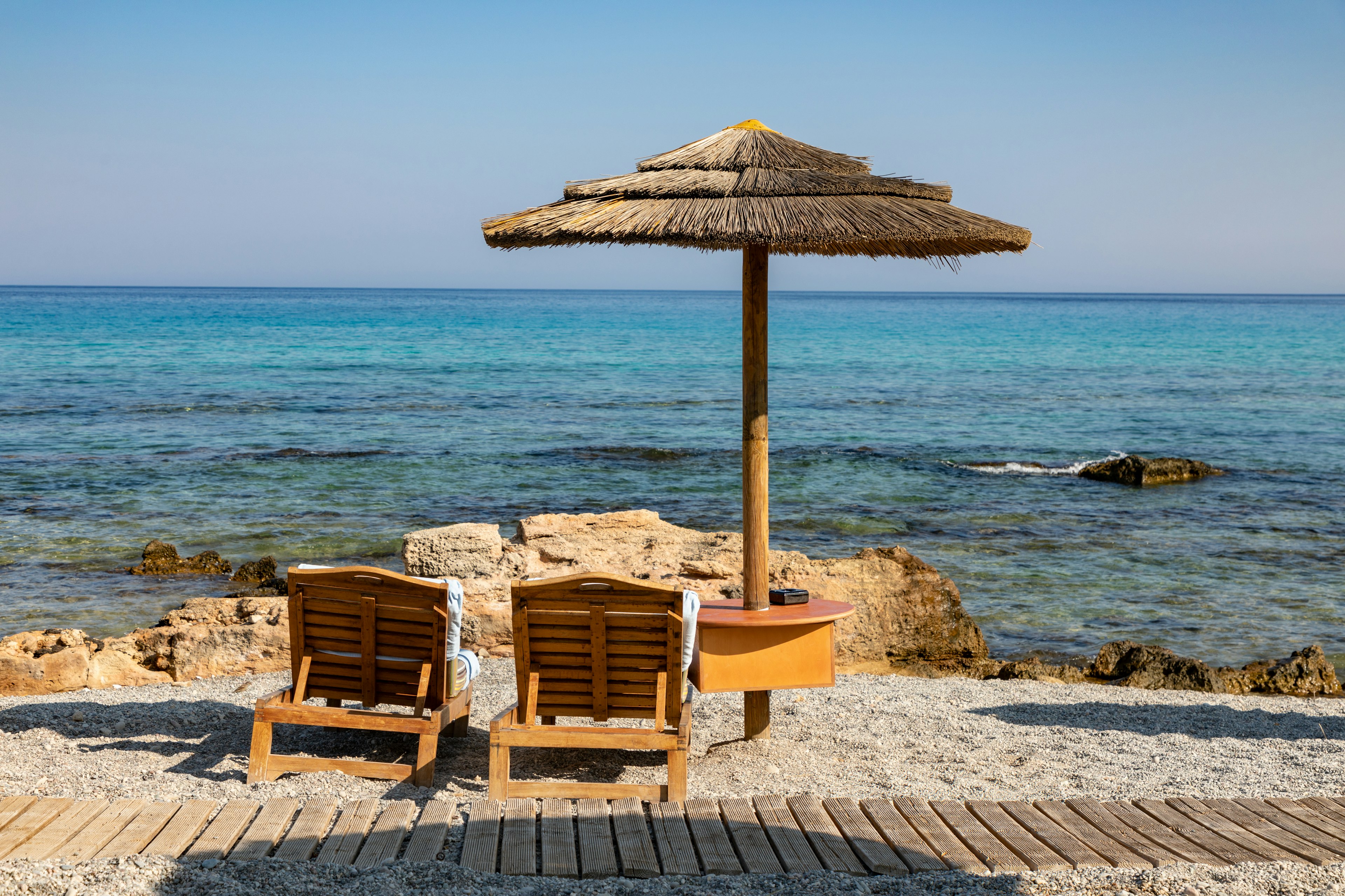 due sdraio di legno sotto a un ombrallone di paglia du una spiaggia di rodi (nell'articolo informazioni e consigli per le vacanze sull'isola)