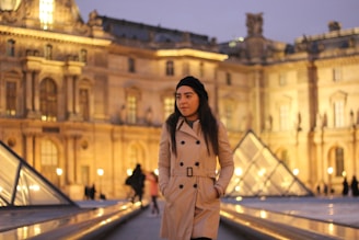 A model wearing a sleek beige trench coat standing on a city street at golden hour