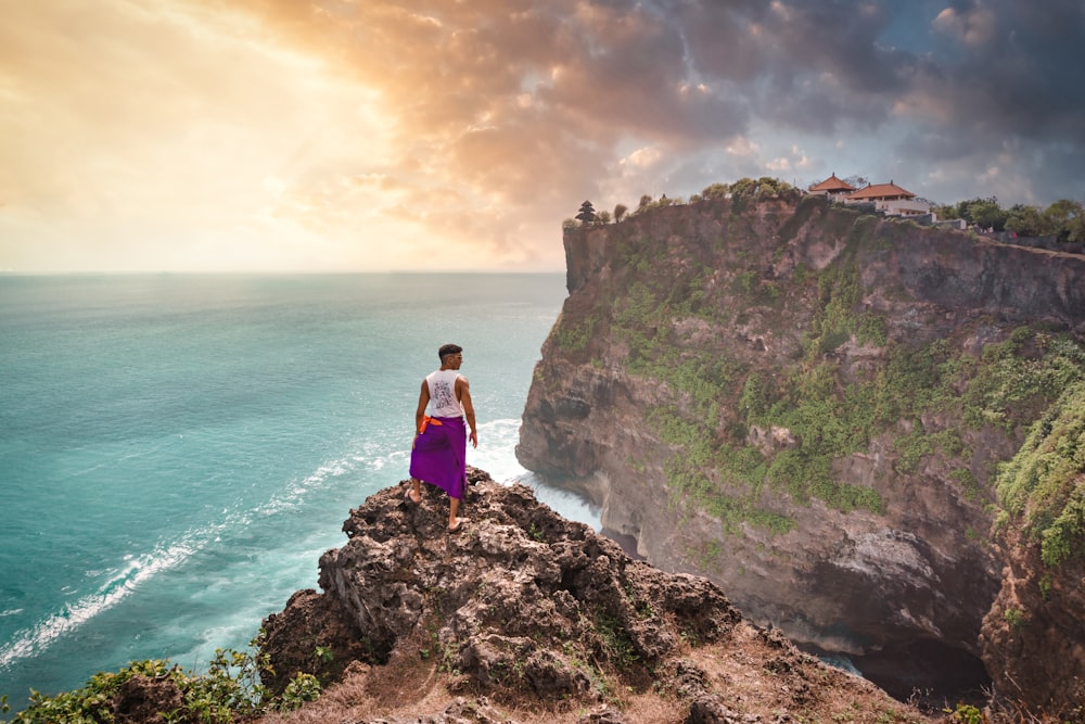 person standing on cliff in front of ocean during daytime