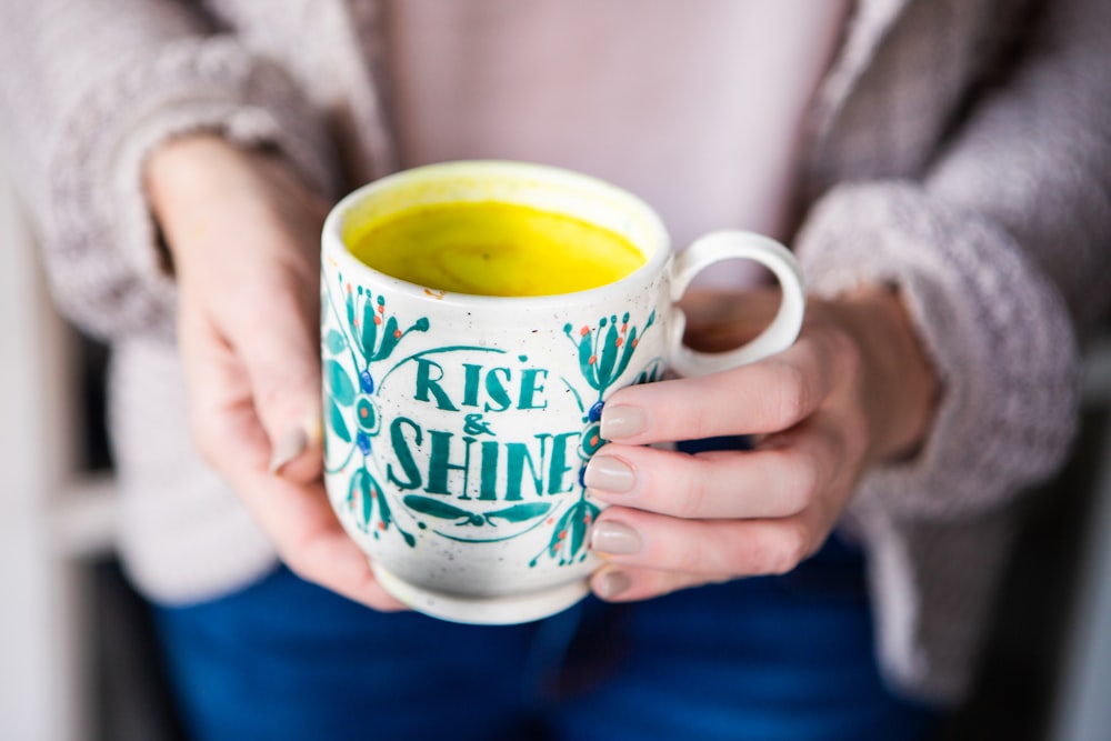 shallow focus photo of yellow liquid in white and teal ceramic mug