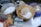 A variety of baking ingredients are arranged on a metallic surface. A large bowl contains oats, cubes of caramel, and white powder, likely flour or powdered sugar. Next to it is a large metal pot with similar white powder. Surrounding the containers are packs of oats, organic salted butter, caramel candies, and a large bag of nuts. A canister of Quaker oats and a salt grinder are also visible.