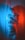 A figure is wrapped in a translucent plastic material, with contrasting blue and red lighting casting colorful shadows and reflections. The printed text on the plastic creates an abstract and slightly industrial appearance.