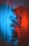 A figure is wrapped in a translucent plastic material, with contrasting blue and red lighting casting colorful shadows and reflections. The printed text on the plastic creates an abstract and slightly industrial appearance.