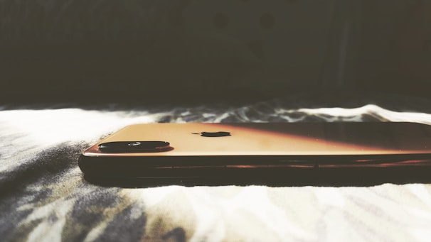 A smartphone with a sleek, metallic finish is lying on a soft, textured surface, illuminated by natural light that casts soft shadows.