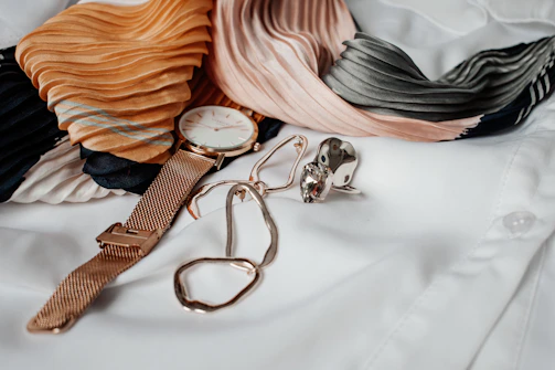 A sleek gold watch resting beside a delicate silk scarf with rich tones.