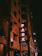The image features the corner of a building at night with a vertical neon sign displaying the word 'PARK' in red lights. The building's facade has a geometric, textured design, and there is a smaller sign at the bottom that reads 'PMI' and 'New York Convenience'. The overall ambiance is dimly lit with an urban, nighttime setting.