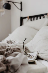 A comfortable double bed with soft pillows and a light throw blanket beside a small reading lamp.