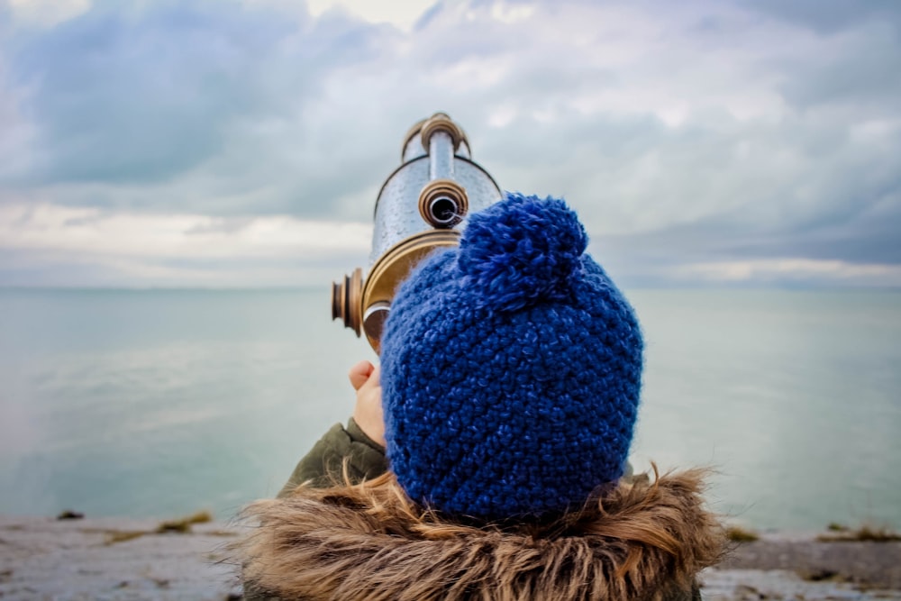 toddle in front of gold and silver telescope on beach