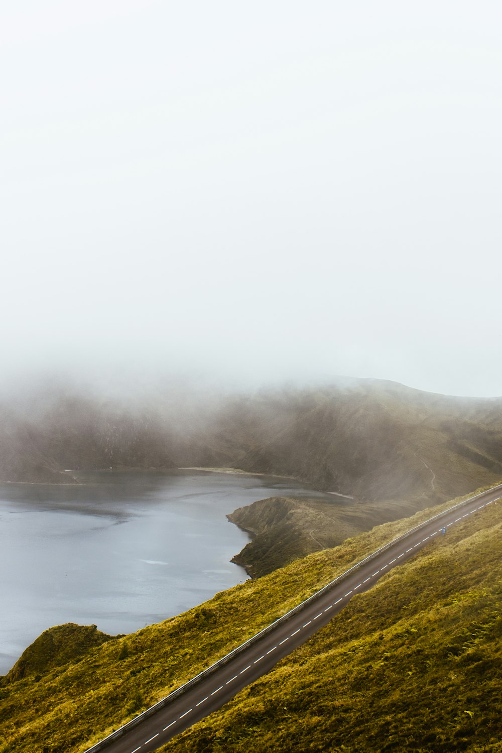 road on top of green grassy hill near lake during daytime