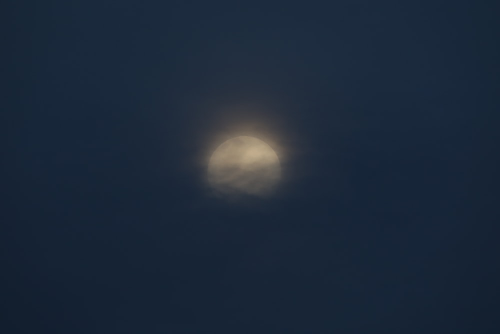 a full moon seen through the clouds in a dark sky